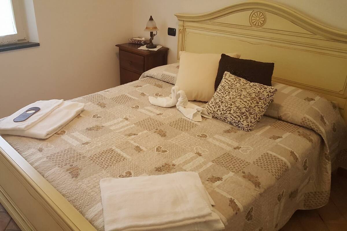 Una cama bien hecha con una colcha estampada, dos almohadas y toallas dobladas.