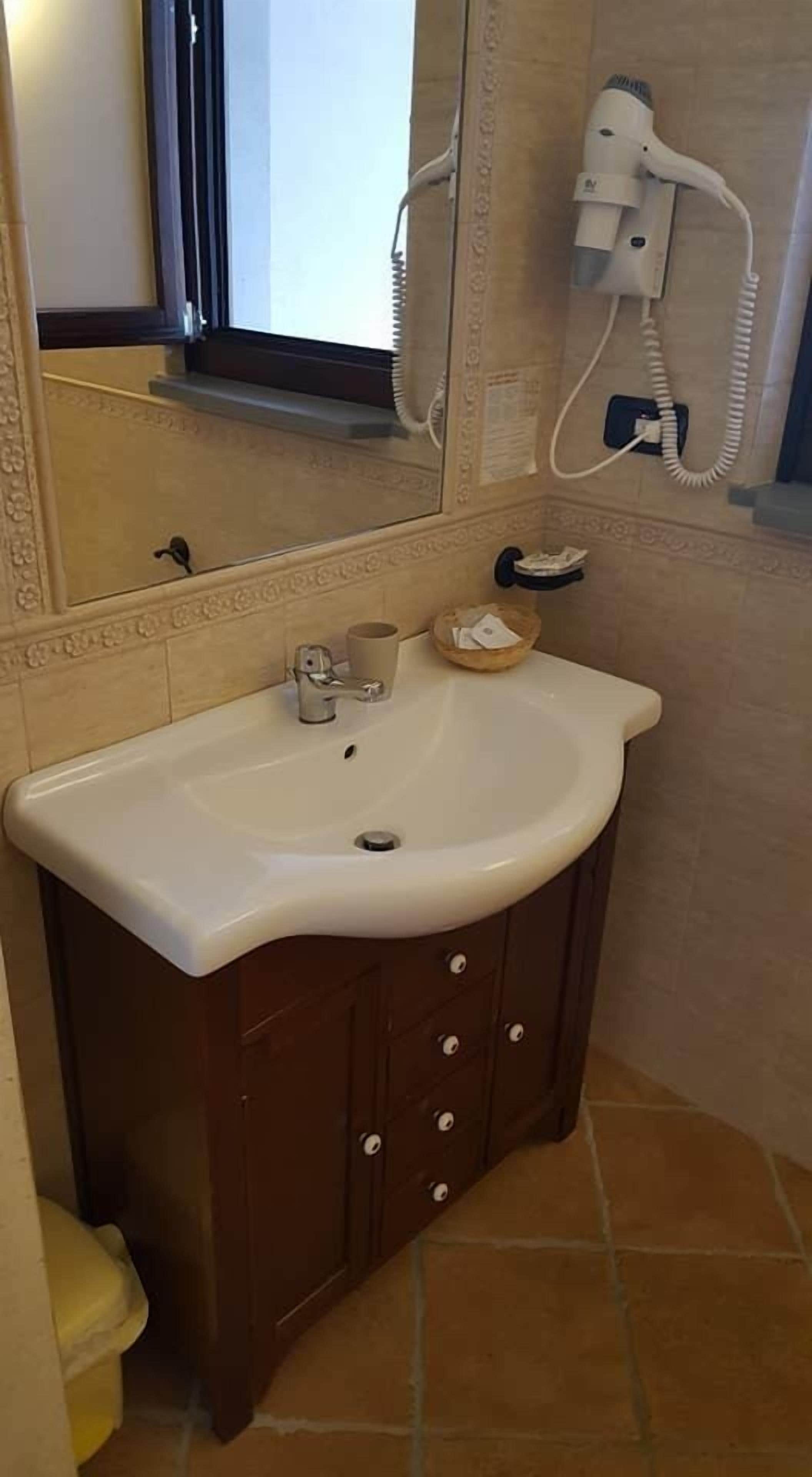 A bathroom with a white sink, a mirror, a hairdryer, and a small basket on the counter.