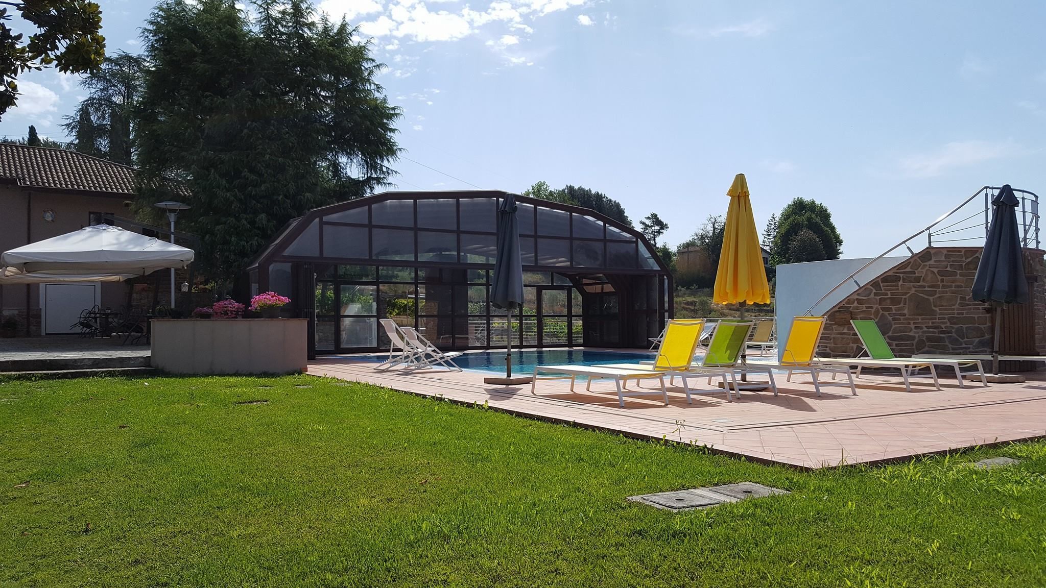 Zona de piscina amb un bany d'hidromassatge envoltat de vidre, gandules i ombrelles.