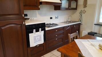 Een keuken met houten kastjes, een gasfornuis, een spoelbak en een eettafel met geruit tafelkleed.