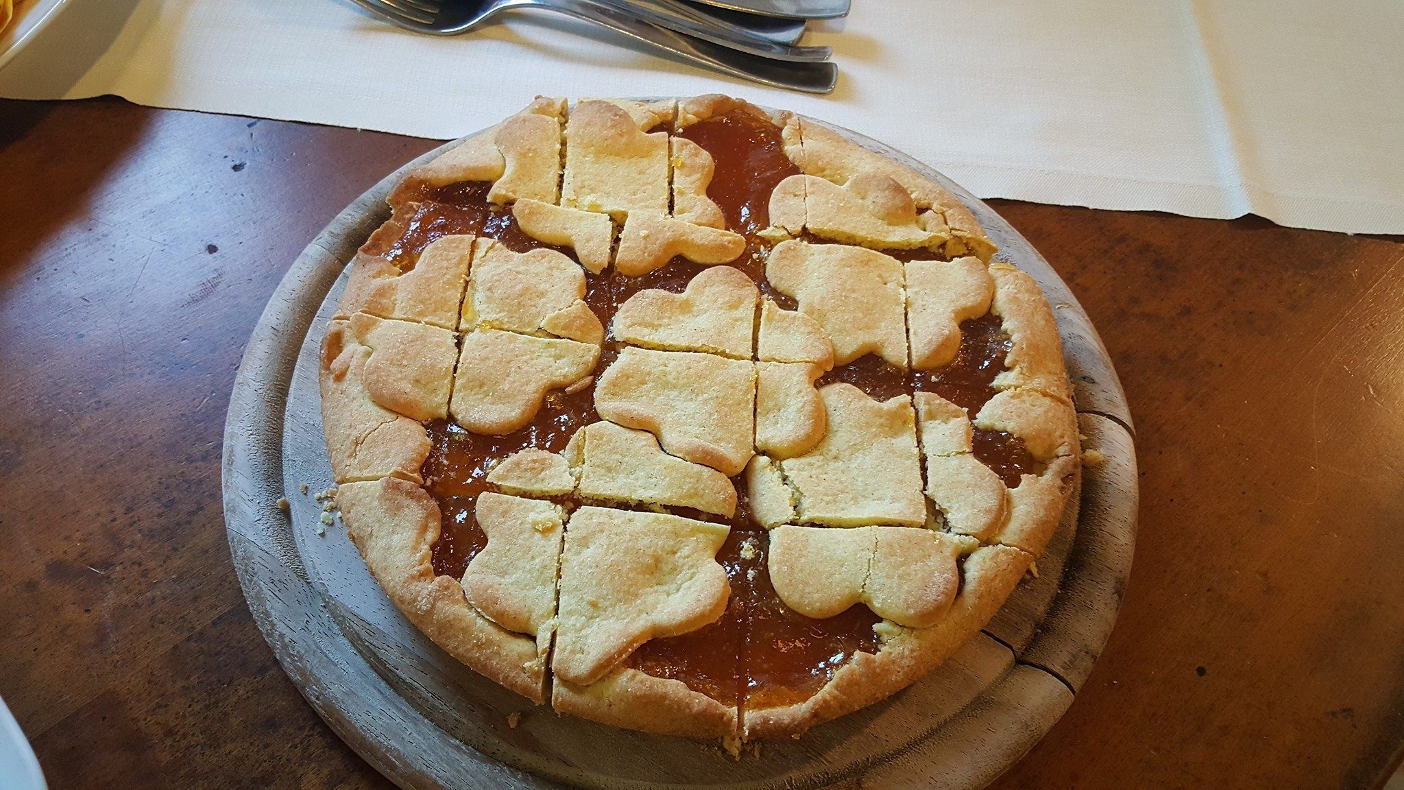 Pyöreä piirakka, jonka päällä on koristeellinen, ristikkomainen kuori, ja se on asetettu puulautaselle.