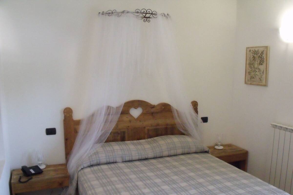 Un dormitorio con cama de madera, dosel blanco, mesita de noche con un teléfono y una lámpara fijada a la pared.