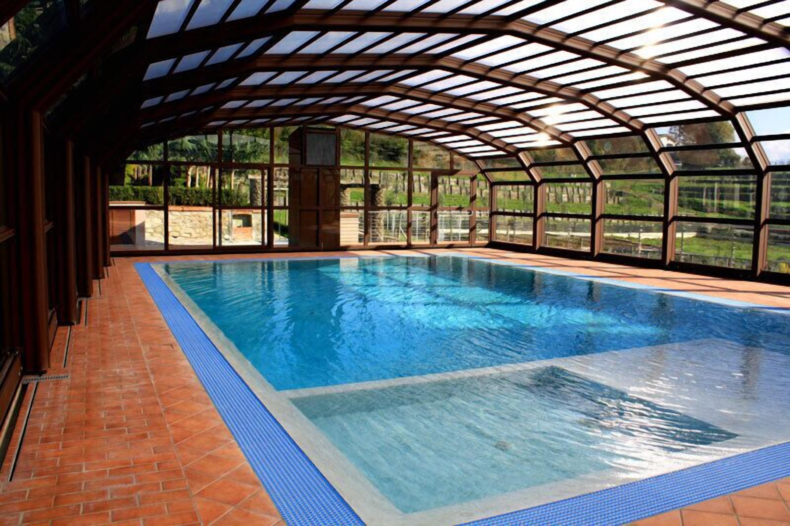 An indoor swimming pool with a glass ceiling, surrounded by a brick floor and stone walls.