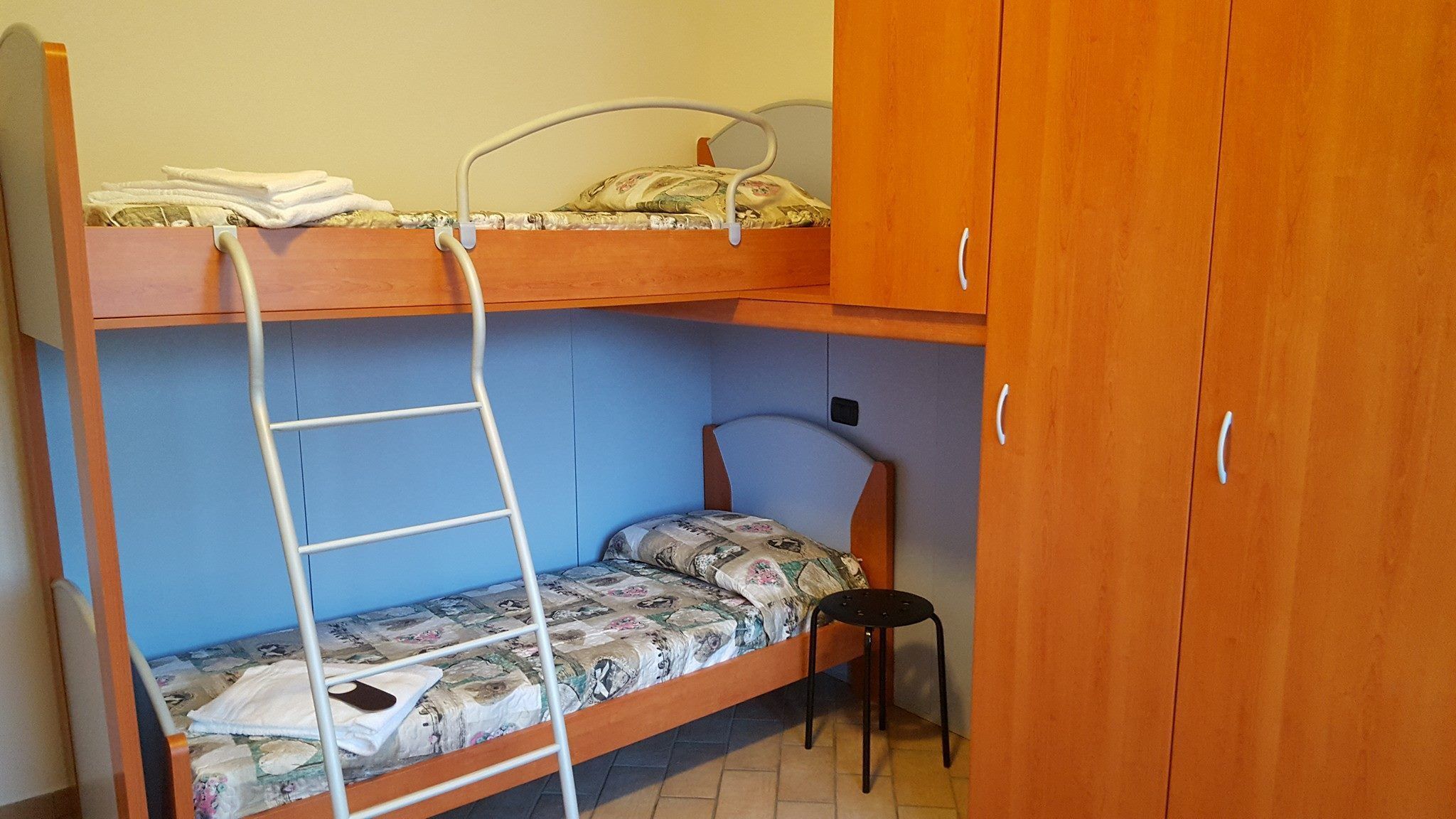 Un letto a castello con una scala, una sedia e un armadio in una stanza dalle pareti blu.