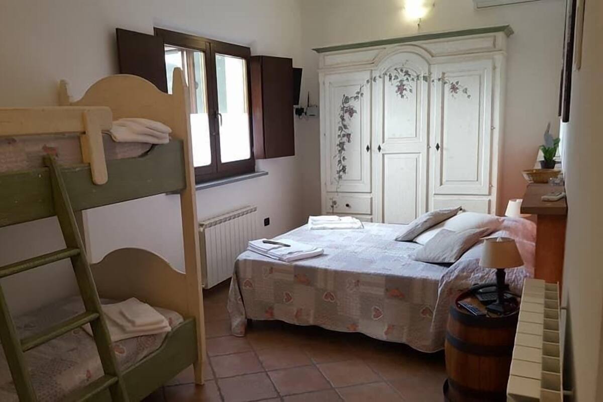 Un dormitorio con una cama litera, una cama individual, un armario, un radiador y una ventana.