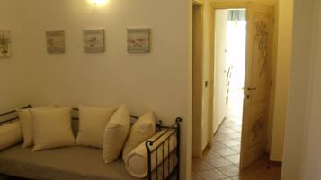 A room with a beige sofa, a wall-mounted light fixture, and a door leading to another room.