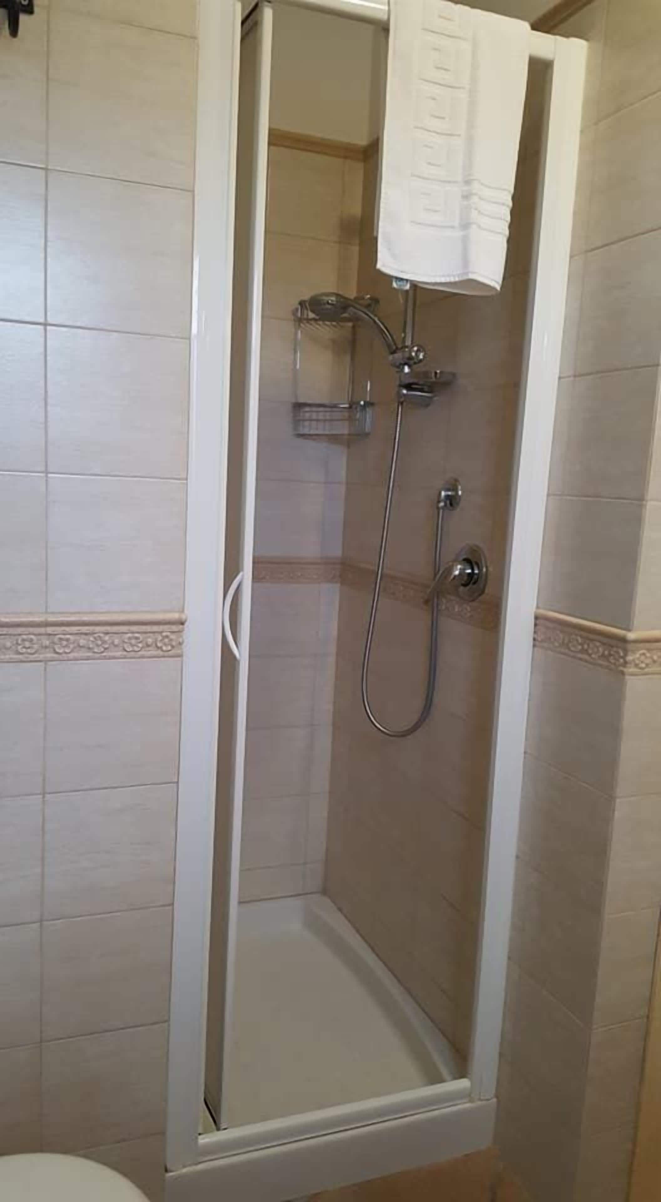 A shower with a glass door, a towel hanging on the door, and a showerhead.