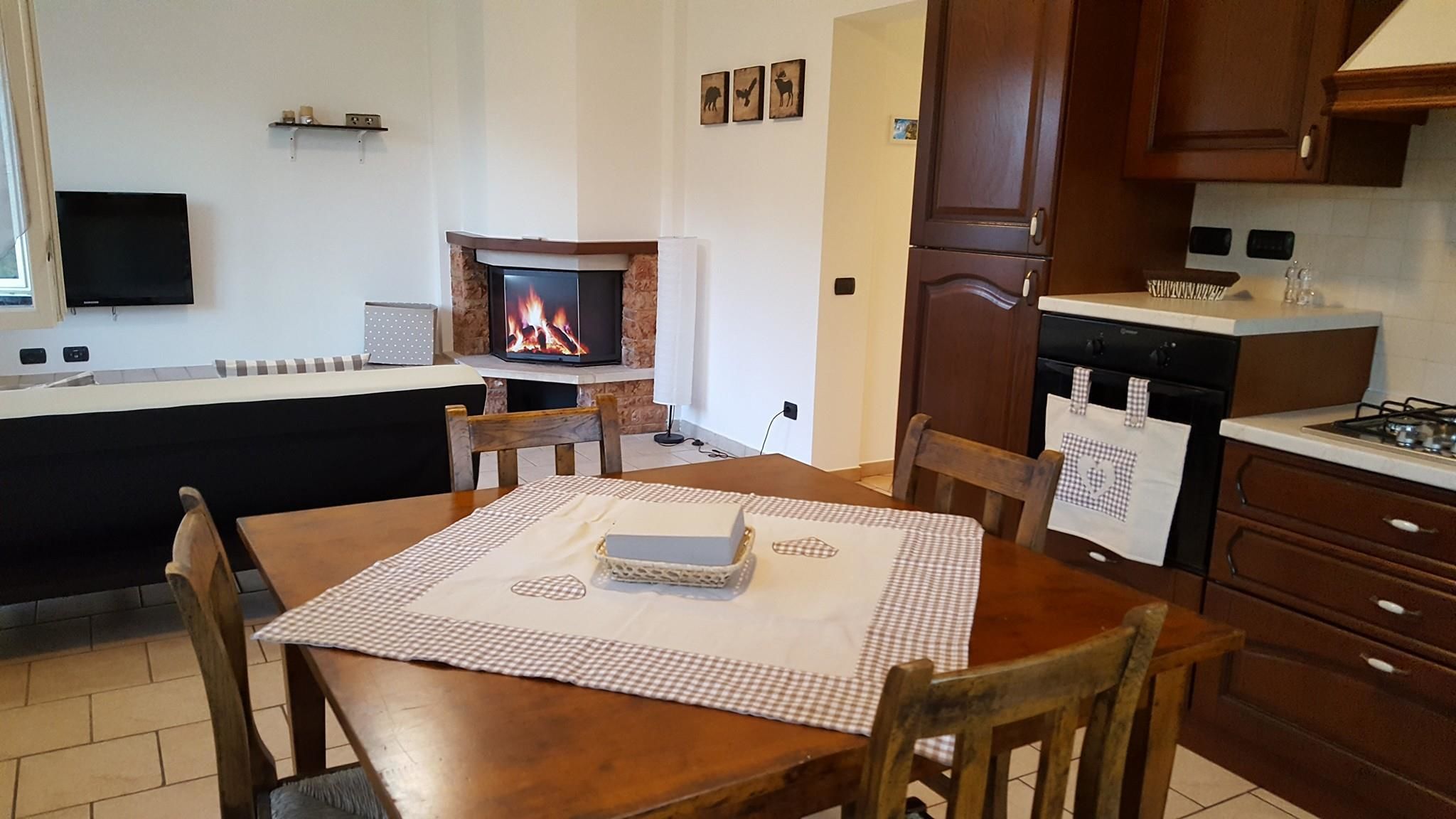 Une cuisine chaleureuse avec une cheminée, des meubles en bois et un coin repas agrémenté d’une nappe à carreaux.