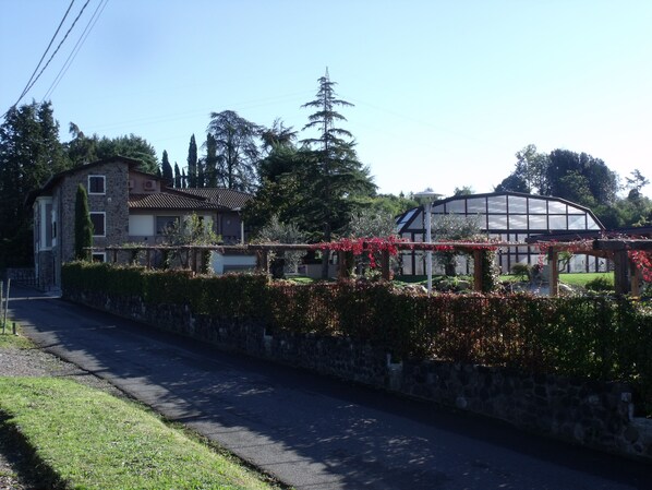 Una casa de piedra con techo de tejas, un invernadero y un muro de piedra con plantas en flor.