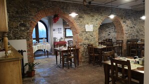 Een restaurant met stenen muren, houten tafels en stoelen. Er zijn twee bogen die leiden naar een andere ruimte.