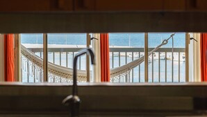 A kitchen with a view of the sea through a window with orange curtains.