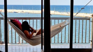A hammock on a balcony with a view of the sea and boats.