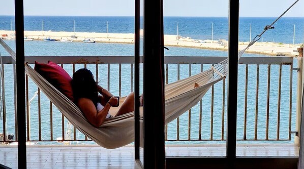 Eine Hängematte auf einem Balkon mit Blick auf das Meer und Boote.