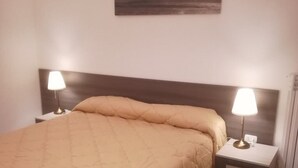 A neatly made bed with a beige quilt, two bedside tables with lamps, and a painting on the wall.