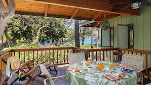 Um deck de madeira com uma mesa posta para o café da manhã, com vista para uma paisagem arborizada e o oceano.