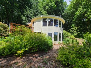 A two-story house with a curved roof, surrounded by dense greenery and trees. - Retreat to wine country (Amity)