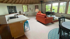A spacious room with a wooden ceiling, a kitchen area with a white countertop, a red sofa, and a dining table with chairs. - Retreat to wine country (Amity)
