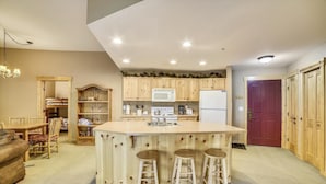 A compact kitchen with wooden cabinets, a central island with stools, a microwave, and a refrigerator. - Tucker Mountain Lodge 102 2 Bedroom Condo by RedAwning (Copper Mountain)