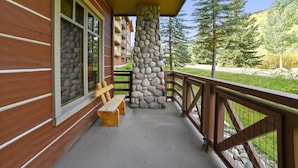A wooden cabin with a stone pillar, a wooden bench, and a balcony overlooking a forested area. - Tucker Mountain Lodge 102 2 Bedroom Condo by RedAwning (Copper Mountain)