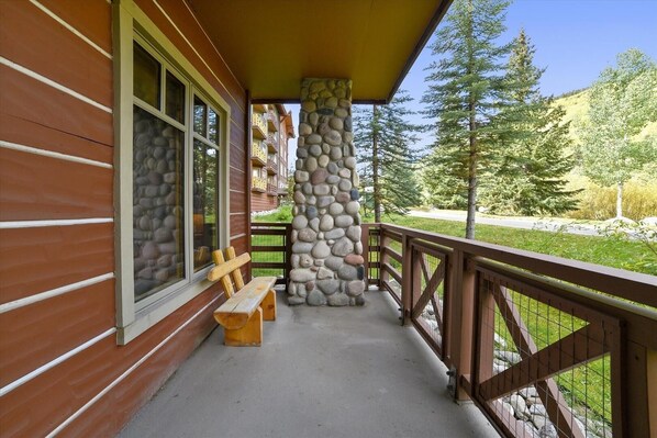 A wooden cabin with a stone pillar, a wooden bench, and a balcony overlooking a forested area. - Tucker Mountain Lodge 102 2 Bedroom Condo by RedAwning (Copper Mountain)