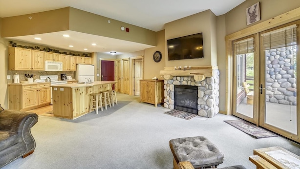 A spacious living area with a fireplace, a kitchen with wooden cabinets, and a stone wall. - Tucker Mountain Lodge 102 2 Bedroom Condo by RedAwning (Copper Mountain)