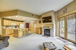 A spacious living area with a fireplace, a kitchen with wooden cabinets, and a stone wall. - Tucker Mountain Lodge 102 2 Bedroom Condo by RedAwning (Copper Mountain)