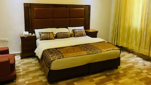 A large bed with a wooden headboard, two bedside tables, and a patterned throw blanket. - Peninsula Hotel & Towers (Lekki)