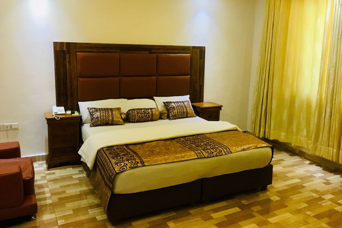 Una cama grande con cabecera de madera, dos mesitas de noche y una manta decorativa.