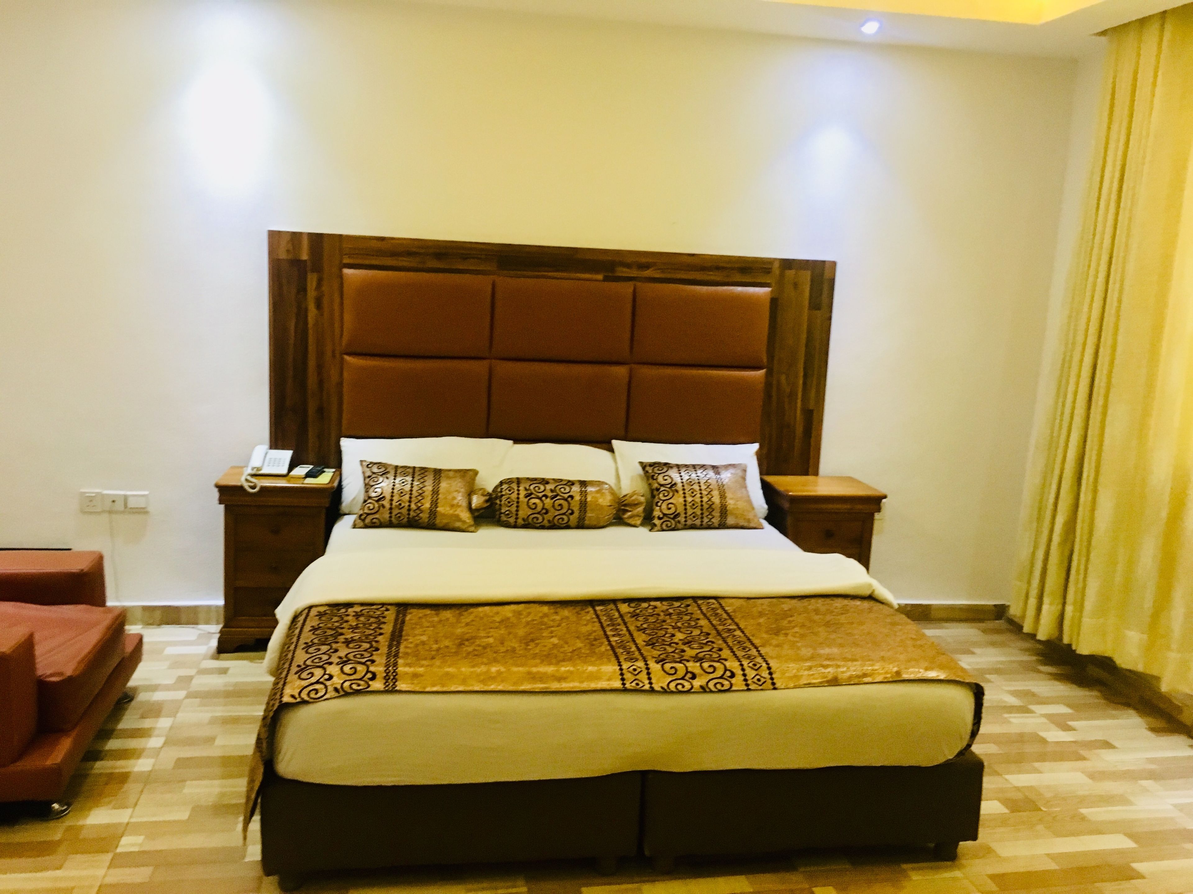 A hotel room with a large bed, a wooden headboard, a bedside table with a phone, and a red armchair.