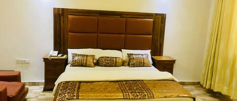 A hotel room with a large bed, a wooden headboard, a bedside table with a phone, and a red armchair.