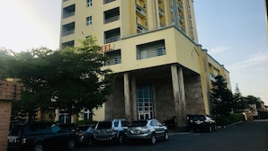 A multi-story hotel with a yellow facade, large windows, and a parking area with several cars. - Peninsula Hotel & Towers (Lekki)
