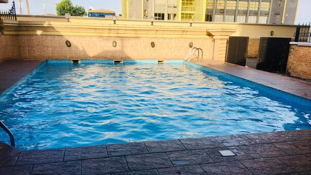 A rectangular indoor swimming pool with clear blue water, surrounded by a tiled deck. - Peninsula Hotel & Towers (Lekki)