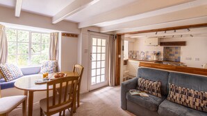 A cozy living room with a dining area, a sofa, and a kitchen visible through an open door. - Cuckoo Tor - Two Bedroom Cottage, Sleeps 4 (Lanteglos)