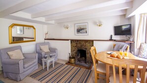 A living room with striped sofas, a fireplace, a television, and a dining area with a table and chairs. - Cuckoo Tor - Two Bedroom Cottage, Sleeps 4 (Lanteglos)