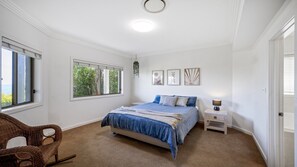 A bedroom with a bed, a chair, a nightstand, and a window with a view of trees.