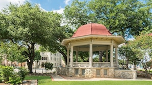 A gazebo with a red dome roof, stone base, and white columns, surrounded by lush green trees and a well-maintained lawn.