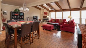A spacious living room with a fireplace, red sofas, and a dining area with a large table and chairs.