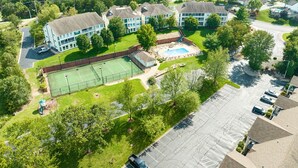 Ett flygbildsbild av ett bostadsområde med en tennisbana, en swimmingpool och flera byggnader.