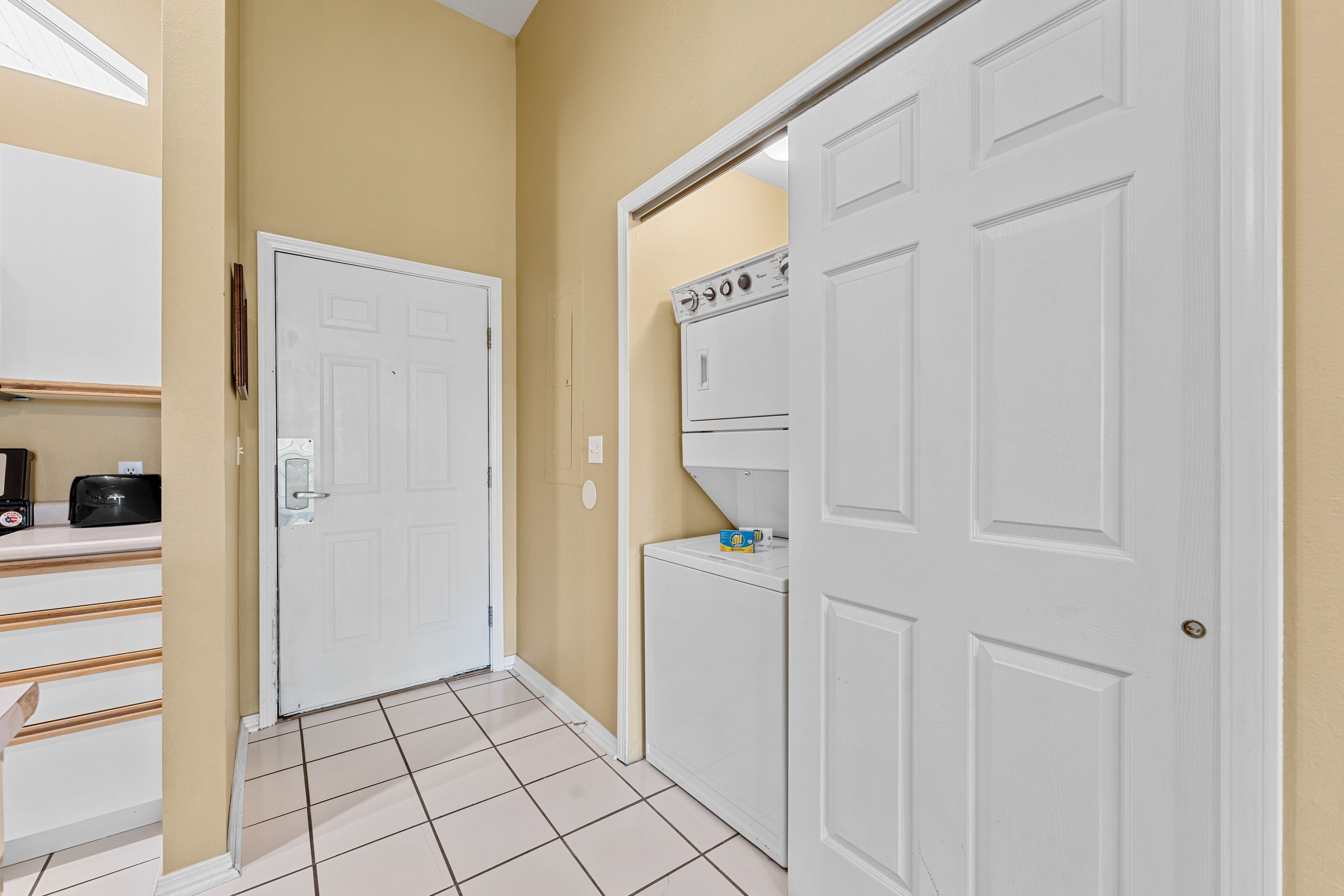A laundry room with a white door, a washer and dryer, and a countertop with a coffee maker and toaster.