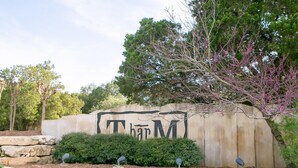 Ein großes Schild mit den Buchstaben "TAM" und ein Baum mit rosa Blüten im Hintergrund.