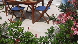 An outdoor dining area with a stone wall, blue shutters, and a table set for four with chairs. - 2-room apartment with terrace 800 meters from the beaches (CANNES)