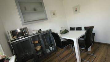 Une cuisine compacte équipée d’un four à micro-ondes, d’un petit meuble avec des portes en verre, d’une table blanche et de chaises noires.