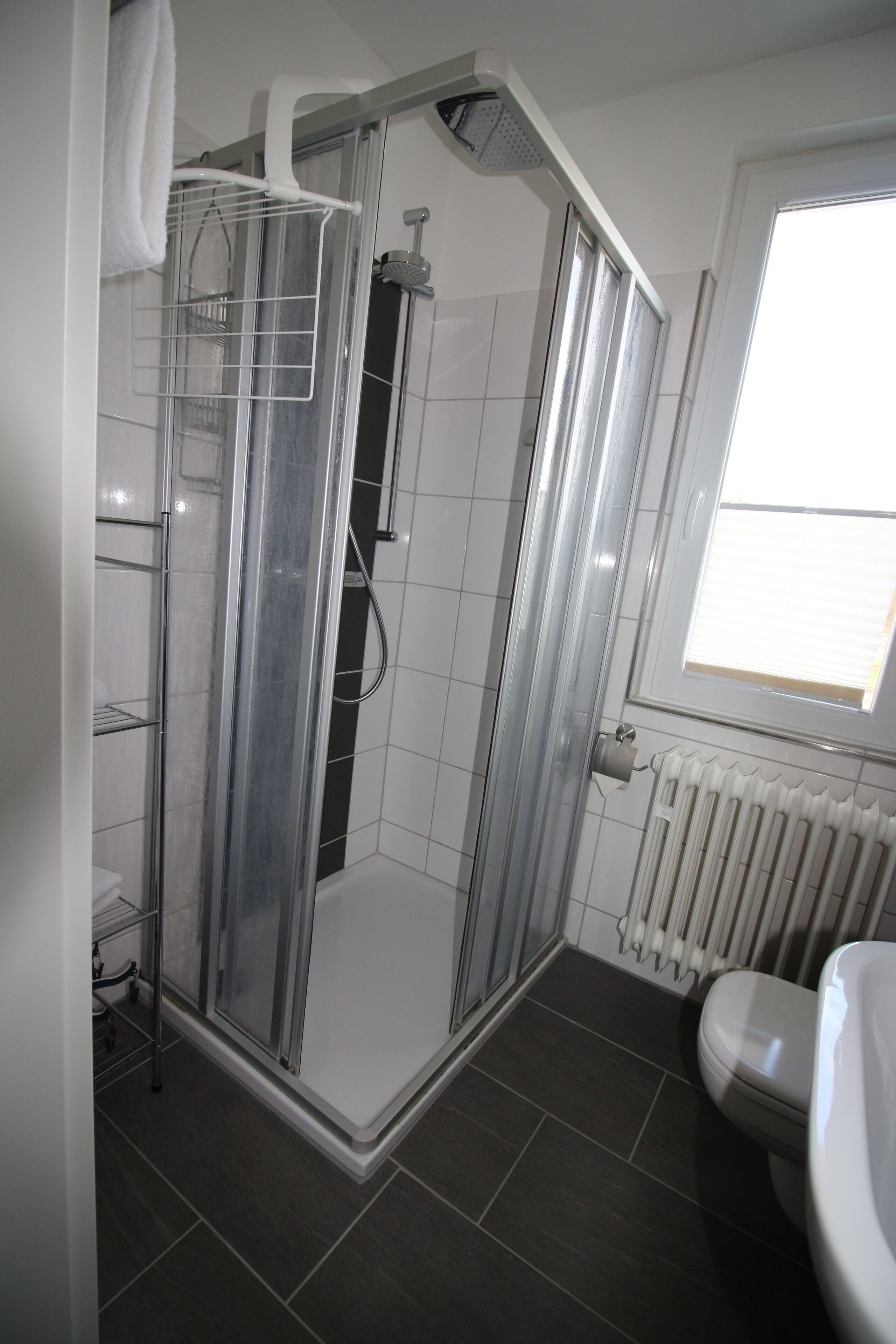 A modern bathroom with a glass-enclosed shower, a toilet, and a window providing natural light.