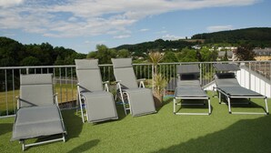 A rooftop terrace with several lounge chairs and a view of a hillside with houses. - Aparthotel Paradies (Bad Salzschlirf)