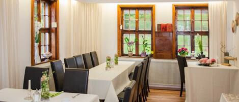 Comedor con varias mesas dispuestas para el servicio, ventanas amplias con cortinas y vistas al exterior con vegetación.