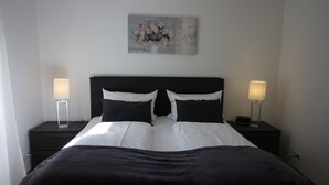 A neatly made bed with a black and white color scheme, two bedside tables with lamps, and a floral artwork on the wall. - Aparthotel Paradies (Bad Salzschlirf)