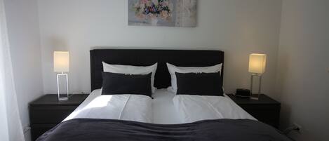 A neatly made bed with a black and white color scheme, two bedside tables with lamps, and a floral artwork on the wall.