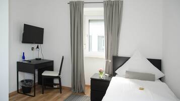 Una habitación de hotel con cama, escritorio, silla, televisor y ventana con cortinas.