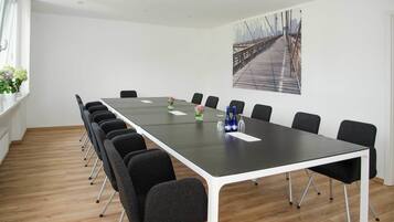 Une salle de conférence avec une longue table, des chaises noires et un tableau représentant un paysage urbain accroché au mur.