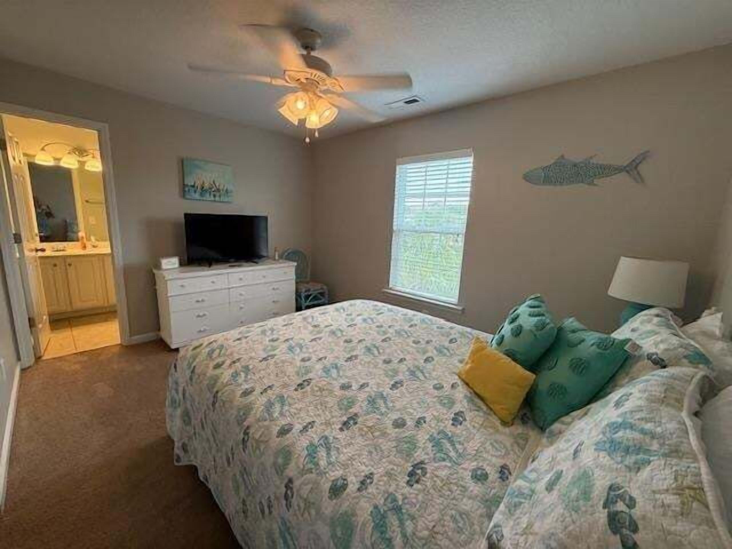 Une chambre à coucher comprenant un lit, une commode, un téléviseur et un ventilateur de plafond.